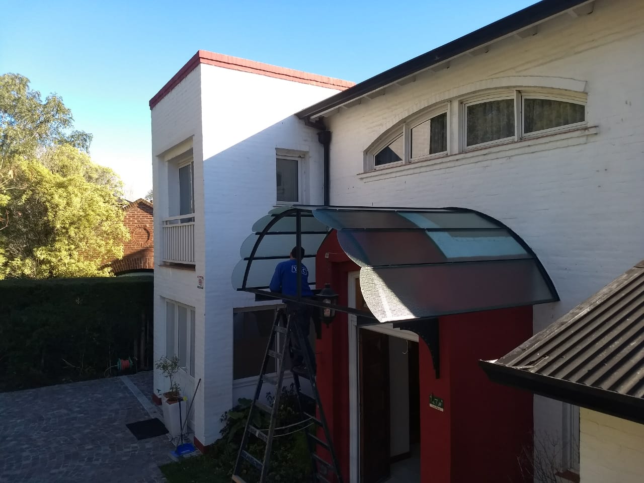 Marquesina curva de vidrio sobre la puerta de entrada de una casa