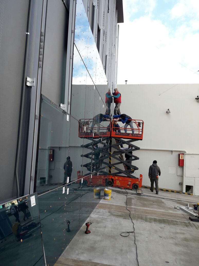 Operarios colocando paños de vidrio en altura desde una plataforma elevadora